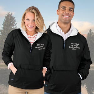 May include: Black hooded anorak jackets with white lining and a front pocket. The jackets have a half-zip closure and the text "Your Text or Logo Embroidered Here" in white. The jackets are worn by two people.