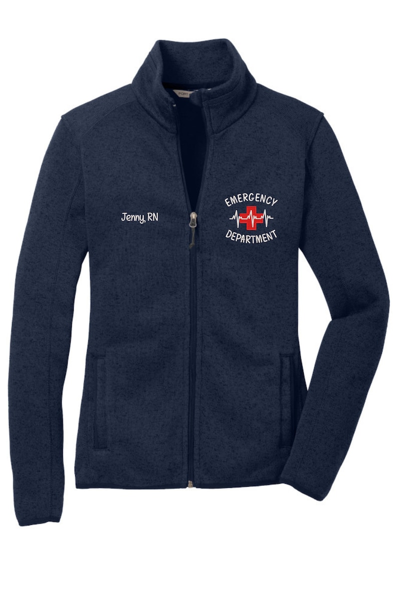 May include: A navy blue fleece zip-up jacket with a white embroidered logo that says "Emergency Department" with a red cross and a heartbeat graphic. The jacket also has a white embroidered name tag that says "Jenny, RN".