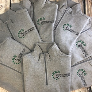 May include: A pile of gray sweatshirts with a green embroidered logo that says "Transforming Architecture".