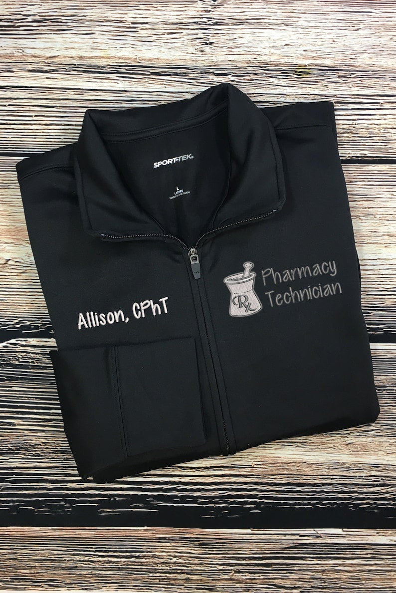 May include: Black zip-up jacket with the text "Allison, CPhT" and "Pharmacy Technician" embroidered in white. A mortar and pestle graphic is also embroidered on the jacket. The jacket is made by Sport-Tek.