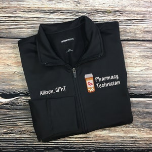May include: Black zippered jacket with a white embroidered design of a pill bottle with the text "Pharmacy Technician" and "Allison, CPhT".