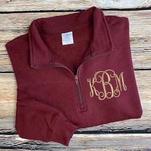 May include: Burgundy quarter-zip sweatshirt with a gold embroidered monogram "KBM" on the front.