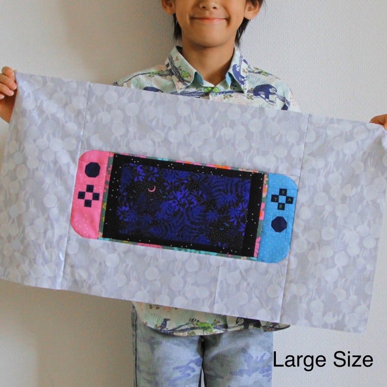 May include: A white fabric pillow with a large, colorful embroidered image of a video game console. The console is pink and blue with a black screen showing a dark blue and purple forest scene. The text "Large Size" is printed in black at the bottom of the pillow.