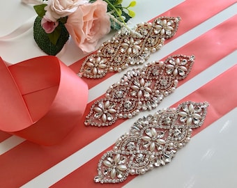 May include: Three coral pink satin ribbons with different rhinestone and pearl embellishments. The embellishments are in the shape of flowers and have a vintage style.