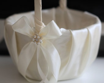 Può includere: Un cestino da damigella d'onore in raso bianco con un ornamento di perle e strass su un fiocco.
