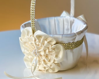 Può includere: Un cestino da damigella d'onore in raso bianco con un bordo di glitter dorato e un grande fiore di raso bianco con un abbellimento di perle.