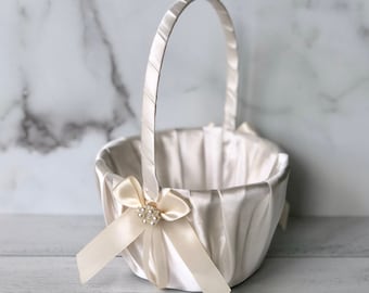 Può includere: Un cestino per damigella d'onore in raso bianco con un design plissettato e un fiocco di nastro di raso con un abbellimento di perle.