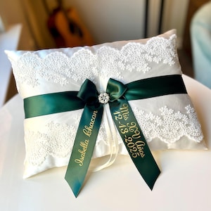 Peut inclure: Un coussin d'alliances en satin blanc avec une bordure en dentelle et un ruban vert fonc&eacute;. Le ruban est orn&eacute; d'un bijou en strass et de deux rubans verts avec le texte dor&eacute; "Isabella Chacon" et "Mis XV A&ntilde;os 12-13-2025".