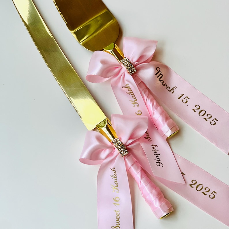 May include: Gold cake cutting knife and server set with pink satin bows and ribbons. The ribbons are personalized with the text "Sweet 16 Kailah" and "March 15, 2025".