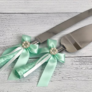 以下が含まれることがあります： ミントグリーンのサテンリボンとパールがあしらわれた、銀製のケーキカットナイフ2本セットです。