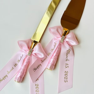 May include: Gold cake knife and server set with pink satin ribbons. The ribbons are tied in bows and have the text "Happy Sweet 16 Kailah" and "March 15, 2025" printed in gold.