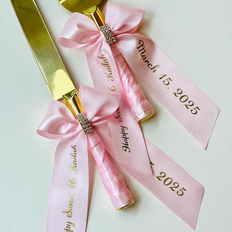 May include: Two gold cake cutting knives with pink satin ribbon bows and gold lettering. The ribbon on one knife says "Happy Sweet 16 Kailah" and the other says "March 15, 2025 16 Kailah".