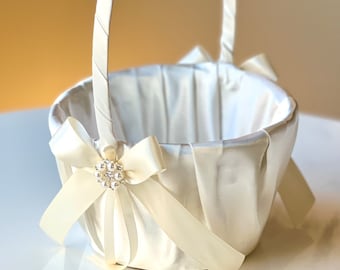 Può includere: Un cestino da damigella d'onore in raso bianco con un ornamento di perle e strass su un fiocco. Il cestino è foderato in raso bianco e ha un manico in raso bianco.