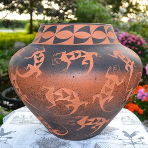 May include: A large, hand-painted terracotta pottery vase with a black and brown glaze. The vase features a geometric design and a repeating pattern of lizards.