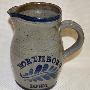 May include: A gray stoneware pitcher with a blue glaze and a blue and white leaf design. The pitcher has the words "Northboro Iowa" on the front.