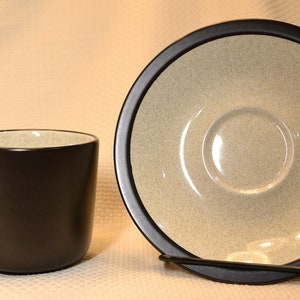 May include: A black ceramic coffee cup and saucer set with a speckled beige interior.