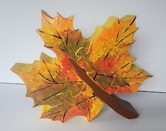 May include: A wooden maple leaf with a brown stem, painted in shades of yellow, orange, and red, resembling autumn foliage.