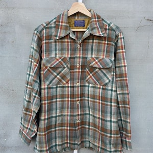 May include: A long-sleeved plaid shirt in shades of brown, green, red, and white. The shirt has two chest pockets and a button-down front. The shirt is hanging on a wooden hanger.