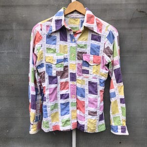 May include: A long-sleeved button-down shirt with a patchwork design. The shirt is made of a white fabric with squares of different colors, including pink, blue, yellow, green, and purple.