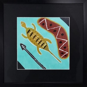 Könnte beinhalten: Gerahmtes Kunstwerk im Aboriginal-Stil. Es zeigt eine gelbe Eidechse mit weißen Punkten, einen braunen Bumerang mit weißen Zickzacklinien und einen schwarzen Speer auf türkisfarbenem Hintergrund. Der Rahmen ist schwarz.