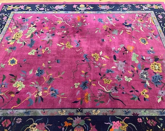 May include: A large, rectangular rug with a vibrant fuchsia field. The rug features a floral pattern with blue, yellow, and green accents. A dark blue border frames the rug, adding a contrasting element to the design.