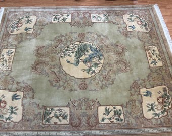 May include: An ornate, rectangular rug with a central medallion featuring a peacock and floral elements in shades of green, blue, and beige. The rug has a detailed border and repeating patterns, with additional floral and bird motifs throughout.