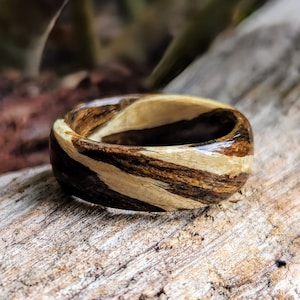 Peut inclure: Une bague en bois avec un motif rayé brun et blanc unique. La bague est faite de bois naturel et a une finition lisse et polie.