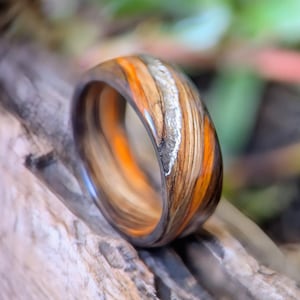 Peut inclure: Une bague en bois au design unique. La bague présente une combinaison de tons orange, marron et argenté. La bague est en bois et a une finition lisse et polie. La bague est un bijou.