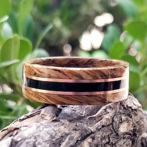Peut inclure: Une bague en bois avec des incrustations noires et cuivrées. La bague est en bois avec un motif de grain naturel. L'incrustation est une fine bande de matière noire avec une bande de cuivre de chaque côté.