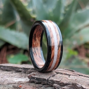 Peut inclure: Une bague en bois noir et brun avec des incrustations blanches. La bague est posée sur une surface en bois.