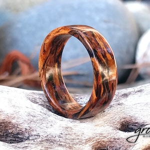 Peut inclure: Une bague en bois avec un motif unique de grain de bois brun et orange. La bague est faite de bois naturel et a une finition lisse et polie.
