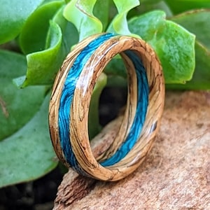 Peut inclure: Une bague en bois avec un incrustation de résine bleue. La bague est faite de bois naturel et présente un motif de grain unique. L'incrustation de résine bleue ajoute une touche de couleur à la bague.