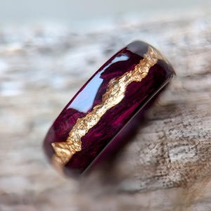Peut inclure: Une bague de couleur pourpre foncé avec une incrustation dorée. La bague est en bois et en résine et a une finition brillante.