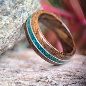 Peut inclure: Une bague en bois avec une incrustation turquoise. La bague est en bois foncé avec un motif de grain naturel. L'incrustation turquoise est sertie dans une bande argentée.