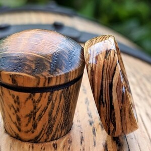 May include: Two wooden rings with a dark wood grain and a clear epoxy finish. The rings are sitting on a wooden surface.