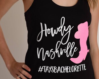 May include: Black tank top with white text that says "Howdy Nashville" and a pink silhouette of a cowboy boot with a hat. The text at the bottom says "#TaysBachelorette".