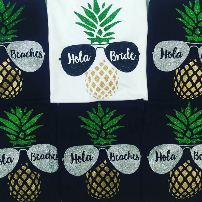May include: Set of six black and white t-shirts with a pineapple design. The pineapples are wearing sunglasses that say "Hola" and "Beaches". One shirt says "Bride" instead of "Beaches".