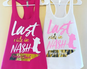 May include: Two white tank tops with the text "Last ride in NASH" in pink and gold glitter. The top on the left is pink and the top on the right is white. Both tops feature a silhouette of a cowboy boot.