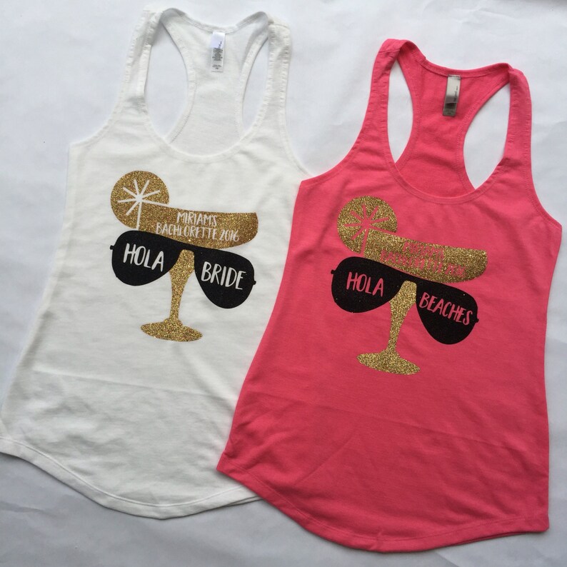 May include: Two white tank tops with a gold glitter margarita glass design. One tank top says "Hola Bride" and the other says "Hola Beaches".