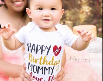 May include: A white onesie with the text "Happy Birthday Mommy" in gold glitter, a red heart with the number 21st in gold glitter, and the text "Love, Eli" in black glitter.