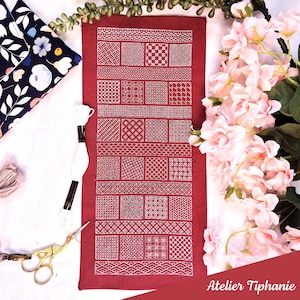 Könnte beinhalten: Ein rotes Textil mit weißem geometrischen Muster, das verschiedene quadratische und rechteckige Designs aufweist. Das Textil ist von Bastelmaterialien umgeben, darunter Faden, Schere und ein Stoff mit Blumenmuster. Der Text "Atelier Tiphanie" ist sichtbar.