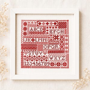以下が含まれることがあります： 白い布にクロスステッチの刺繍が施された正方形の白い額縁。刺繍は赤い糸で、幾何学模様、縁取り、AからZまでのアルファベット、1から9までの数字が長方形のセクションに配置されています。