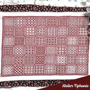 Könnte beinhalten: Ein weißer Stoff mit einem Gitter aus weinroten Quadraten, die jeweils ein einzigartiges geometrisches Muster aufweisen. Der Stoff ist von einem Blumendruck umrandet, und der Text "Atelier Tiphanie" ist unten sichtbar.