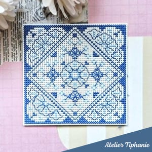 May include: A square cross-stitch design in blue and white. The pattern features floral and geometric motifs within a diamond shape. The design is on a white background, with the text "Atelier Tiphanie" in the bottom right corner.