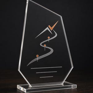 May include: A clear acrylic award with an irregular geometric shape and a rectangular base. The surface features a printed graphic of a stylized gray swooping line, three small orange circles, and an orange checkmark symbol at the top.