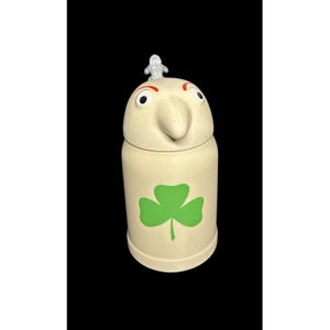 May include: A cream-colored ceramic jar with a whimsical face and a green shamrock design. The jar has a large nose, red eyebrows, and a silver-colored decorative top. The jar is likely a decorative kitchen item.