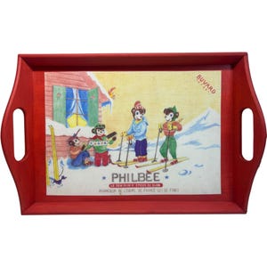 May include: A rectangular red wooden serving tray with cut-out handles. The tray features a vintage illustration of cartoon skiers in a snowy landscape with the text "PHILBEE" and "BUVARD".