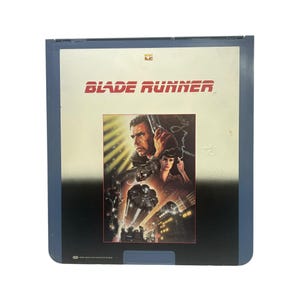 May include: A vintage Blade Runner movie case. The case is blue and black, with the movie title in red. The cover art features Harrison Ford and Sean Young, with a futuristic cityscape.