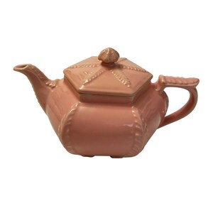May include: A salmon-pink ceramic teapot with a hexagonal body and a matching lid. The teapot features a raised rope-like texture along the edges and a central finial on the lid. It has a curved spout and a handle with a textured top surface.