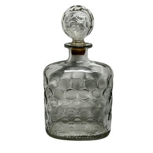 May include: A clear glass decanter with a round, textured stopper. The decanter has a honeycomb pattern on the body and a cork stopper. The design is simple and elegant, suitable for storing and displaying spirits or other beverages.